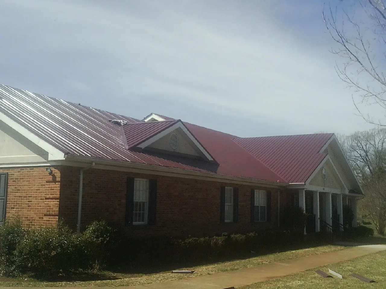 Red metal roof with gabled entries on a long brick building, from a Hail Damage Roof Repair job in Wyoming